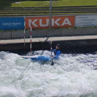 Paddler im blauen Kayak kämpft gegen die Strömung auf einer Wildwasserstrecke, umgeben von spritzendem Wasser.