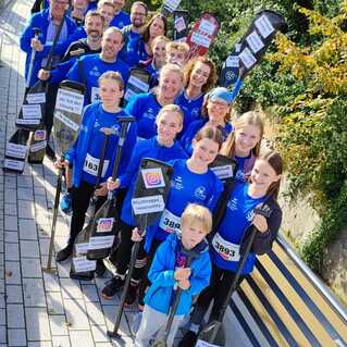 Gruppe von Menschen in blauen Shirts hält Paddel mit Schildern, posiert im Freien an einem Gehweg.