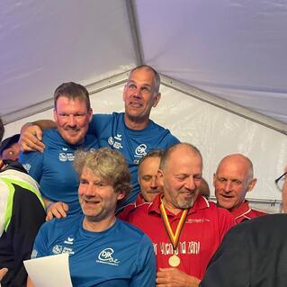 Gruppe von Männern in Sportoberteilen lächelt und posiert in einem Zelt, einige tragen Medaillen.