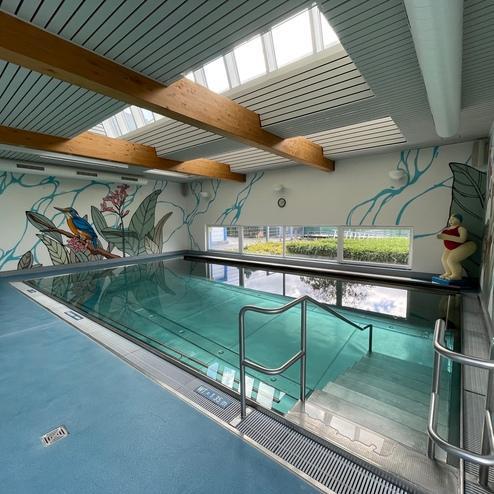 Innenpool mit glasklarem Wasser, umgeben von bunten Wandmalereien und großen Fenstern für Tageslicht.